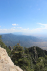 Photo of a yellowish cliff and green trees in the foreground and a range of mountains in the background